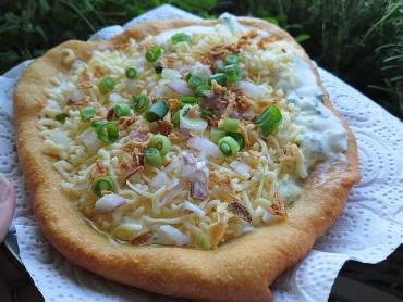 Freshly baked langos topped with sour cream, green onion and grated cheese